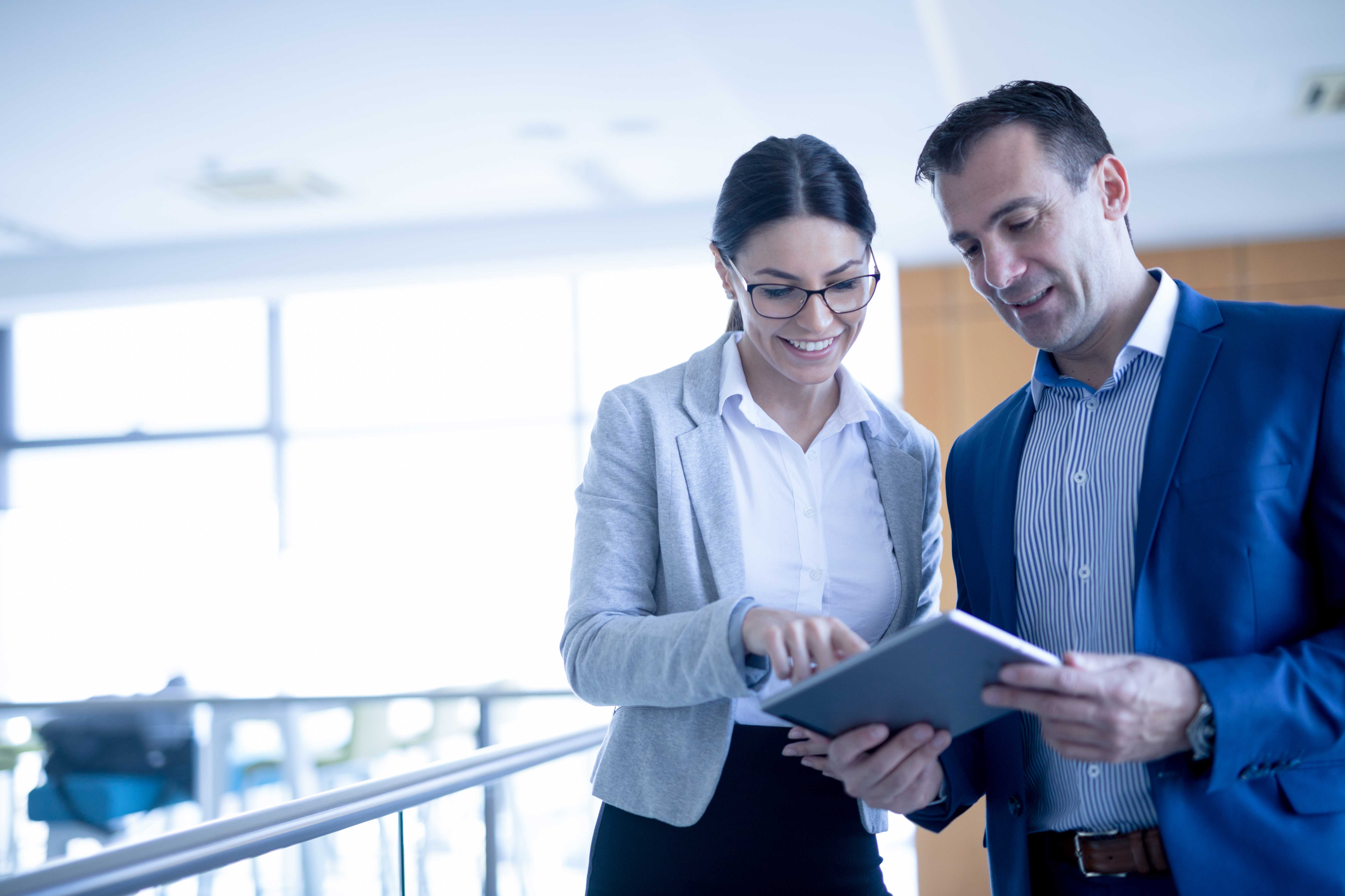 Automatisation de la comptabilité fournisseurs - Deux professionnels d'âges différents discutant d'une stratégie commerciale dans un bureau en regardant une tablette numérique